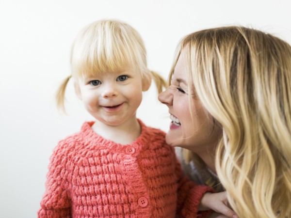 Cute girl (2-3) smiling at camera with mother