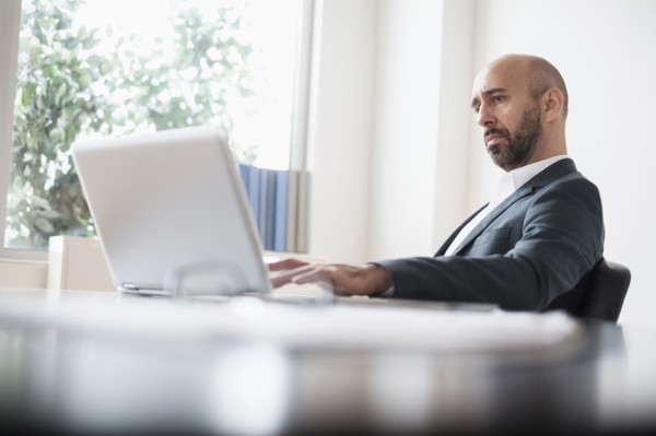 Concentrated businessman working with laptop at desk in office.
