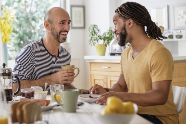Smiley homosexual couple having breakfast in kitchen.
