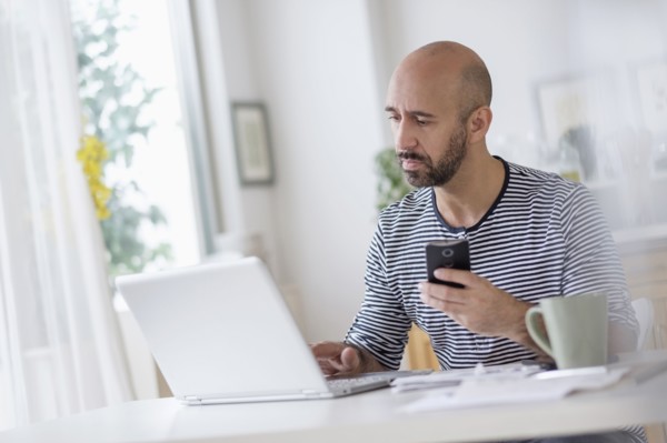 Man working with laptop and holding smart phone at table.