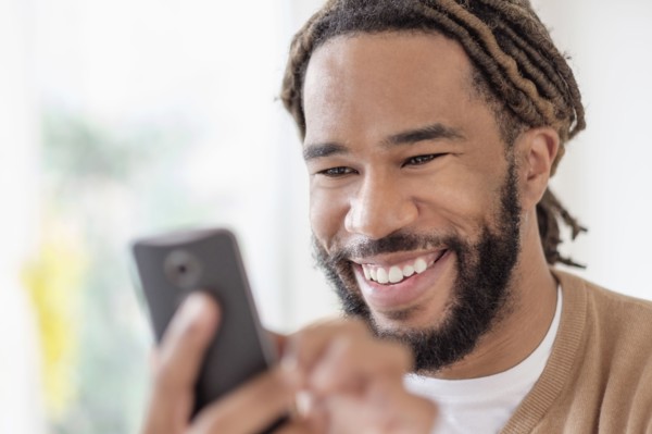 Smiley young man with dreadlocks using smart phone.