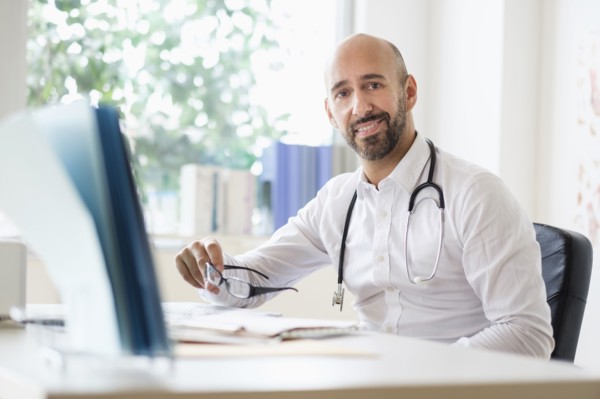 Portrait of smiley doctor working with laptop at desk in office.