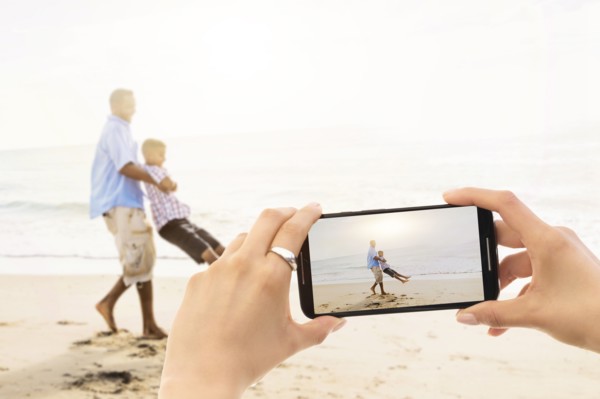 Young woman photographing father with son (12-13) on beach. Jupiter, Florida, USA.