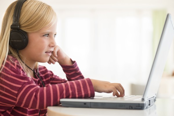 Girl (6-7) wearing earphones, using laptop