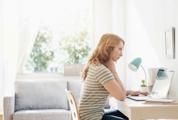 Side-view of young woman working on laptop at home.
