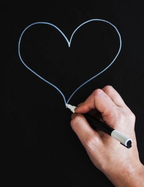 Man's hand drawing heart shape on black paper