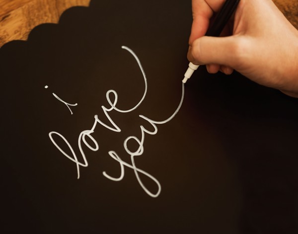 Man's hand writing I Love You on black paper
