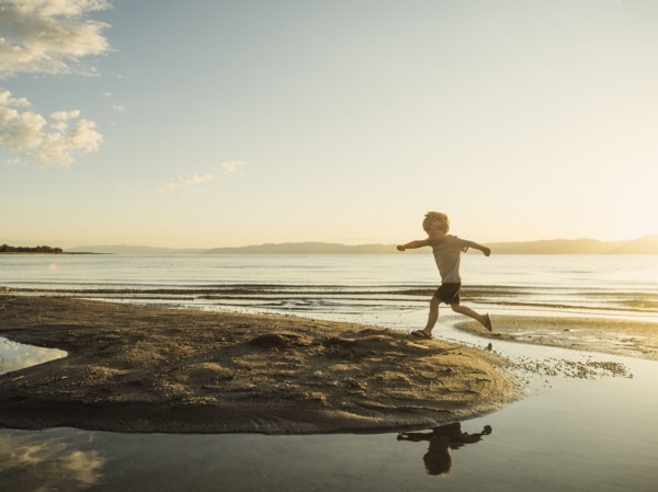 Small boy (4-5) jumping over water on sunny day
