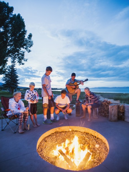 Parents with children (8-9, 10-11, 16-17) sitting in front of campfire and playing guitar