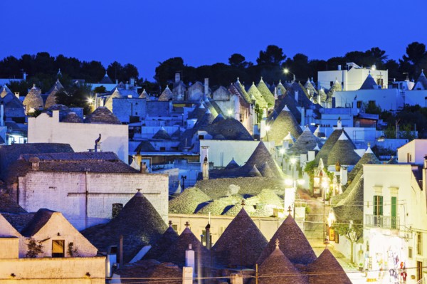 Trulli houses along illuminated street under blue sky