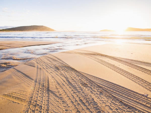 Tire tracks on beach at sunset