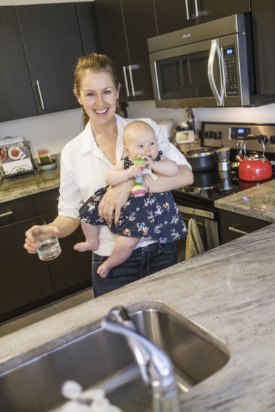 Smiling mother holding baby daughter (2-5 months) and glass of water.