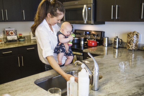 Mother holding baby daughter (2-5 months) and filling glass with water.