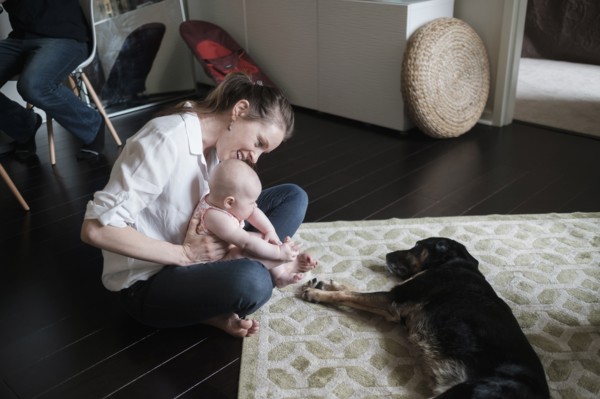 Mother holding baby (2-5 months) and playing with dog.