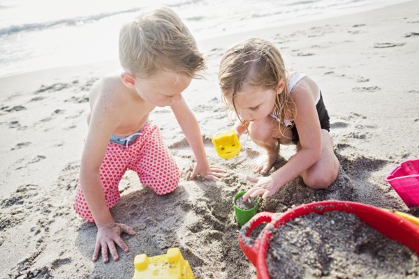 Boy (6-7) and girl (4-5) playing with sand on beach
