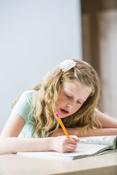 Blonde girl (8-9) doing homework at table