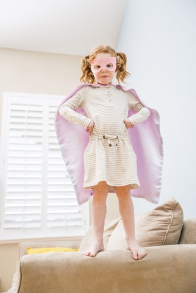 Little girl (4-5) playing superman on sofa