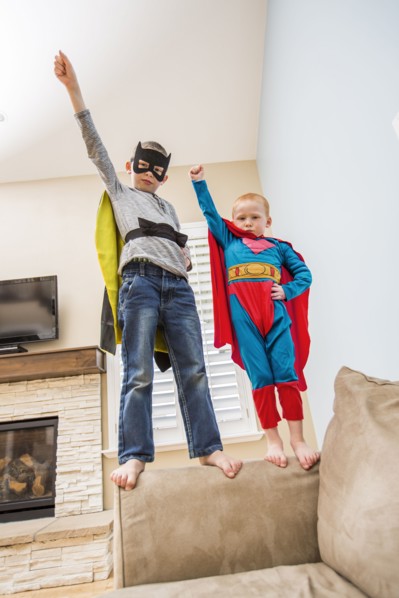 Boys (2-3, 6-7) wearing superhero costumes standing on sofa