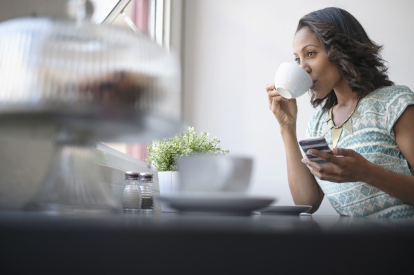 Woman drinking coffee and using phone.