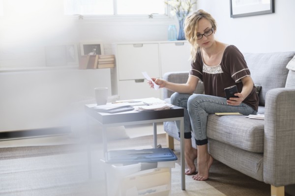 Woman sitting in living room and paying bills using electronic banking.