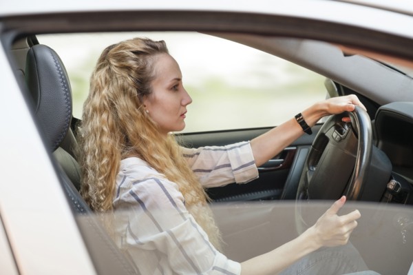 Woman with curly, long, blond hair driving car.