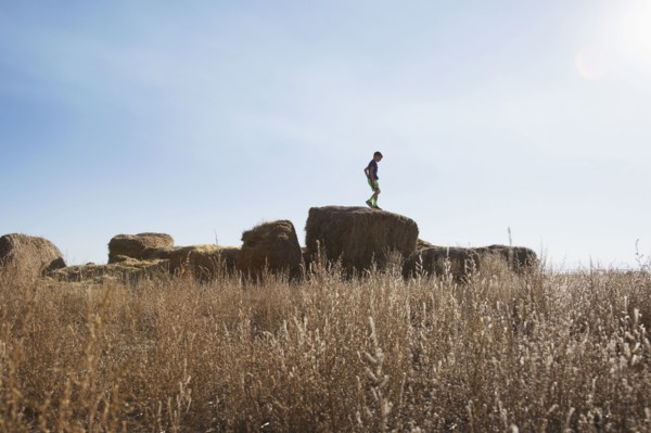 Boy (6-7) standing on bale of hay