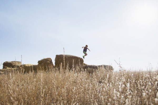 Boy (6-7) jumping on bale of hay
