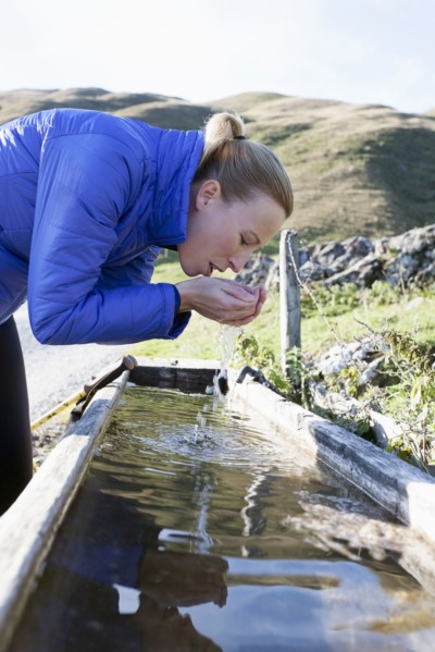 Austria, Salzburger Land, Weissbach, Mature woman drinking water from old wooden drinking trough