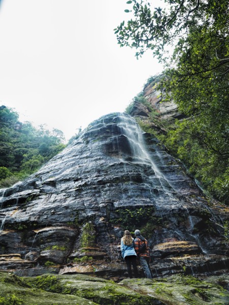 Australia, New South Wales, Blue Mountains National Park, Leura Cascades, Mid-adult couple at foot of rock with waterfall in forest