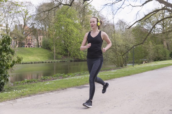 Mid-adult woman with headphones on jogging by canal in park