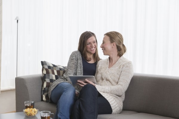 Smiling women sitting on sofa in living room and holding tablet
