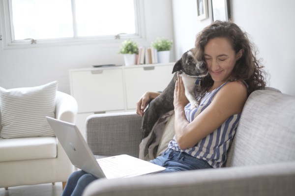 Young woman with laptop cuddling with her dog on sofa.