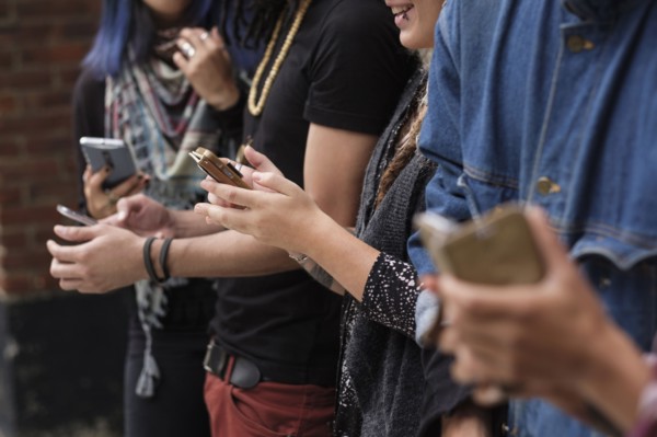 Young people standing in row using smartphones.