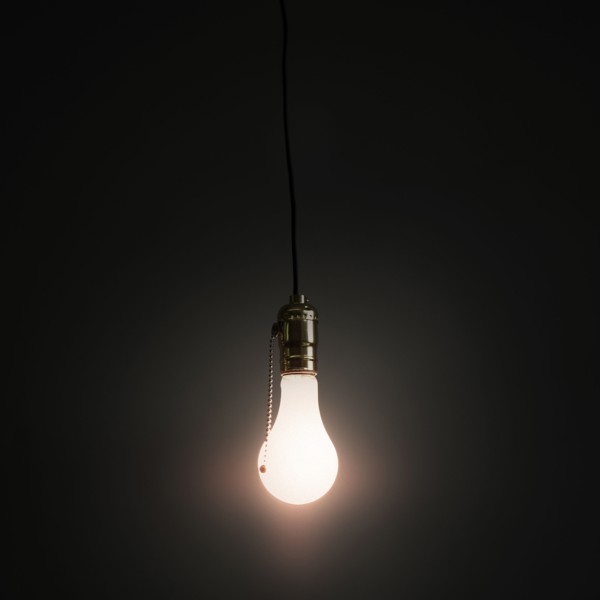 Light bulb hanging against grey background.