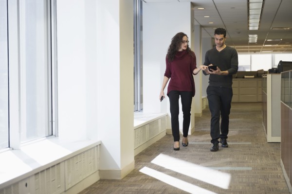 Young people walking side by side in corridor with digital tablet.
