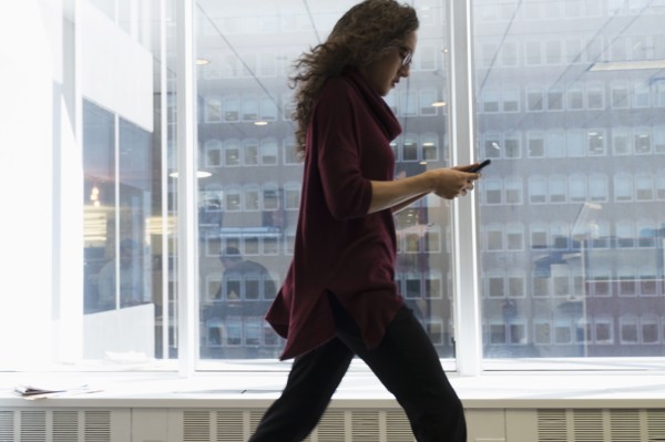Young woman walking with mobile phone in front of window.