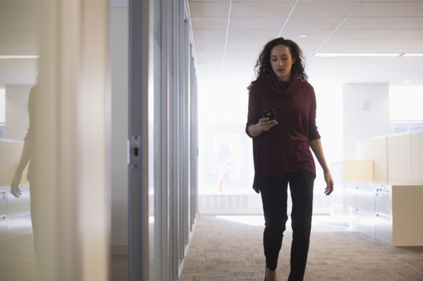Young woman walking in corridor with mobile phone.