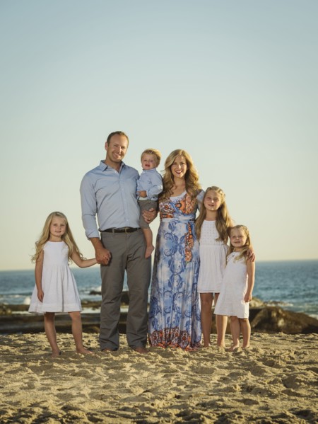 Family with children (12-17 months, 4-5, 6-7, 8-9) standing on beach with sea in background