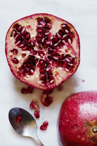 Halved Pomegranate and spoon against white background
