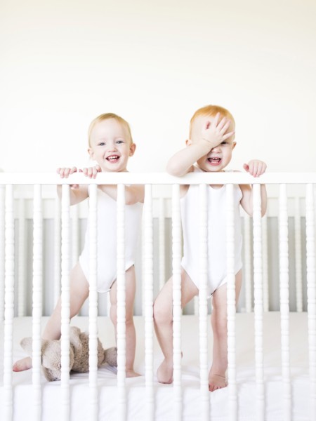 Twin brothers (12-17 months) standing in crib