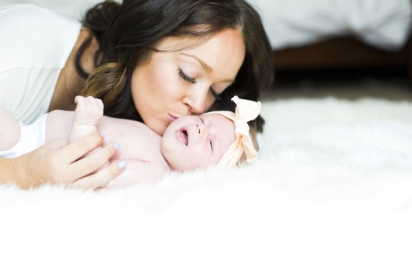 Mother kissing daughter (0-1 months) on bed