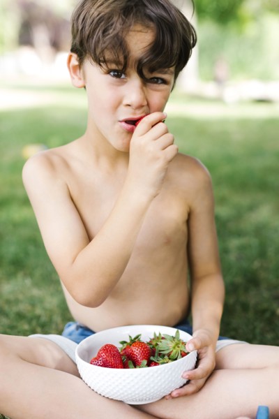 Boy (6-7) sitting on grass and eating strawberry in park