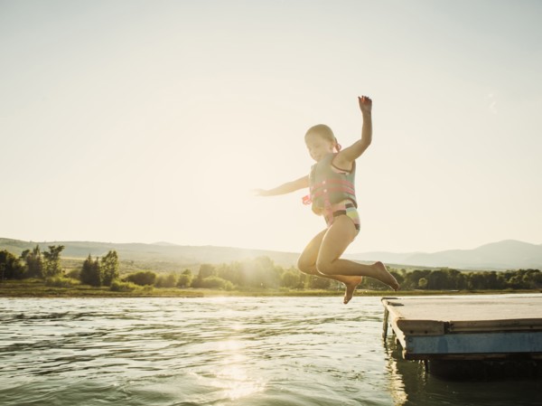 Girl (4-5) jumping into lake from pier