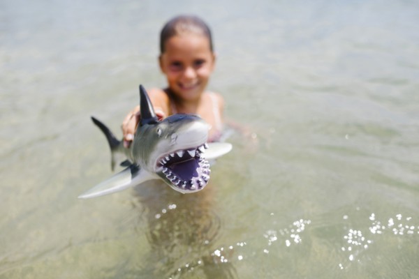 Girl (6-7) playing with toy shark in sea