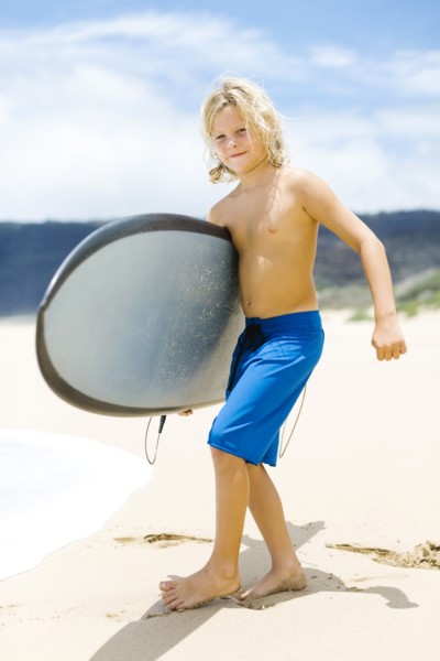 Boy (8-9) standing on beach and holding surfboard