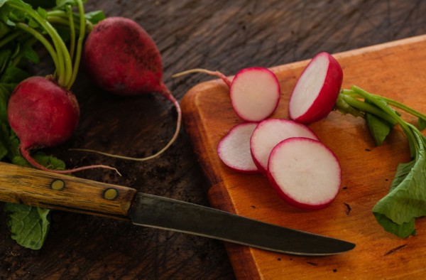 Slices of red radish and knife on cutting board
