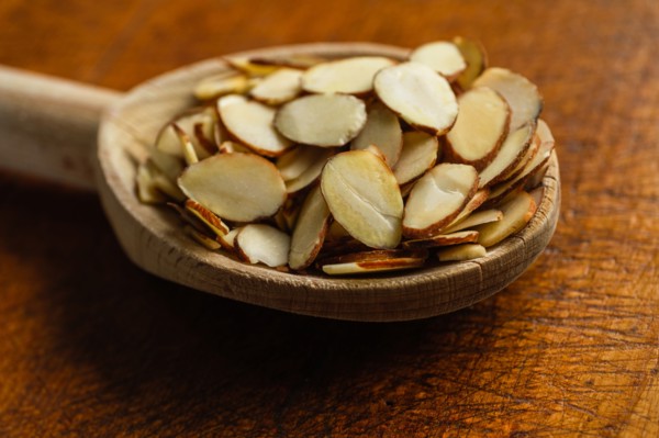 Wooden spoon full of sliced almonds on table
