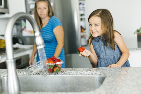 Mother looking at daughter (6-7) holding strawberry in kitchen