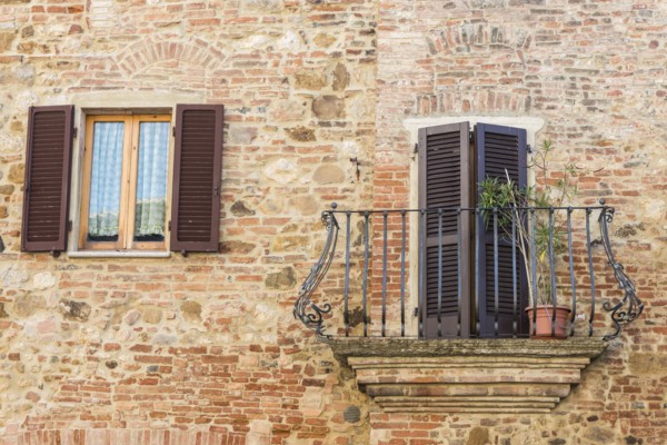 Italy, Tuscany, Montepulciano, Stony and brick facade of house with carved metal balcony and latticed sun blinds