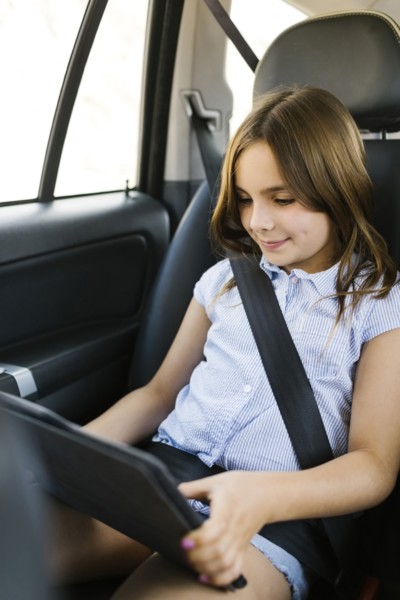 Girl ( 8-9) sitting in car and using digital tablet